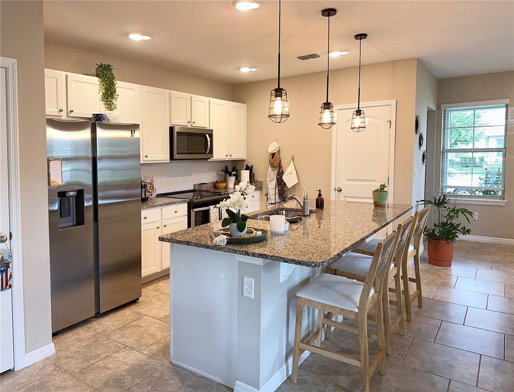 A kitchen features white cabinets, stainless steel appliances, a granite-topped island, and pendant lighting — 10126 SALT POINT DRIVE, WINTER GARDEN, FL