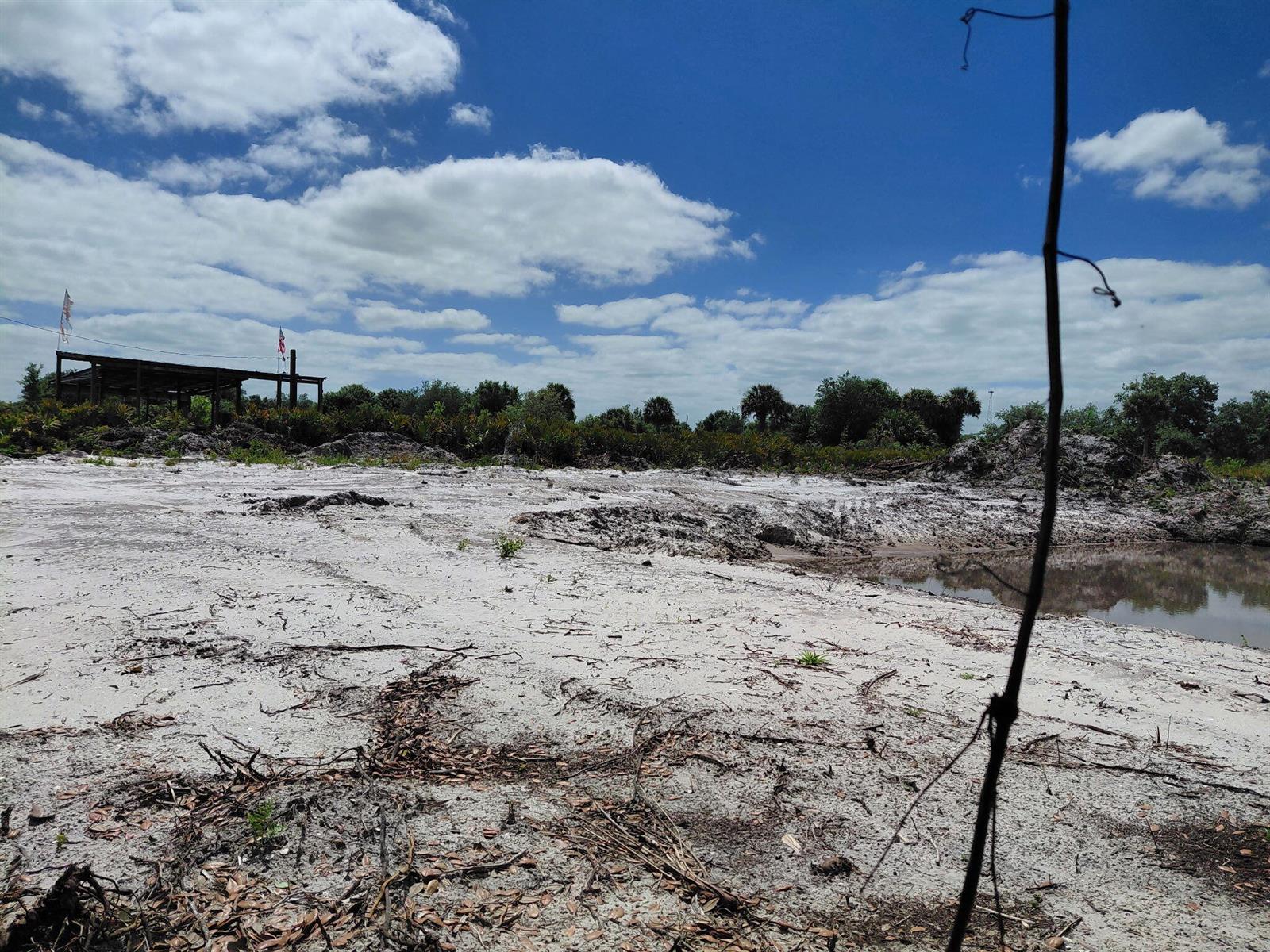 A cleared, sandy lot features a small pond and a distant, partially constructed wooden structure — 17122 NW 292nd Street, Okeechobee FL 34972, OKEECHOBEE, FL