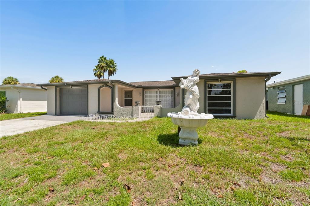 A single-story house with a garage, a front lawn, and a decorative statue fountain — 7407 POPULUS DRIVE, PORT RICHEY, FL