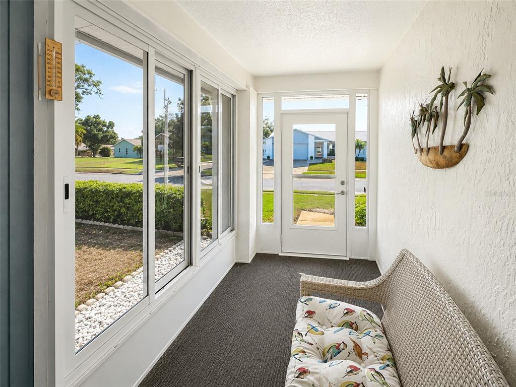 A sunroom features large windows, a white door, dark carpeting, and a wicker bench — 2942 MACALPIN DRIVE W, PALM HARBOR, FL