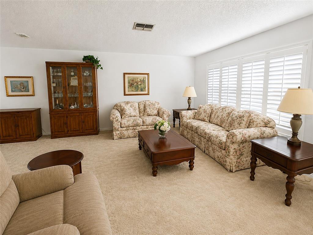 A living room with beige carpet, floral sofas, a recliner, and a wooden coffee table — 2942 MACALPIN DRIVE W, PALM HARBOR, FL