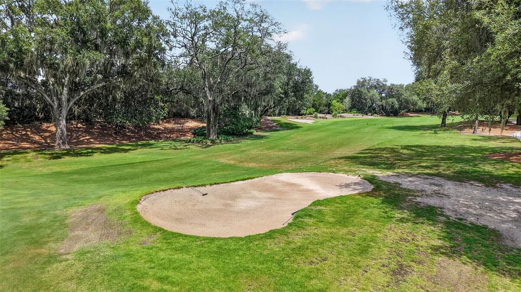 A sand bunker sits in the foreground of a green golf course lined with trees — 522 LOMA PASEO DRIVE, LADY LAKE, FL