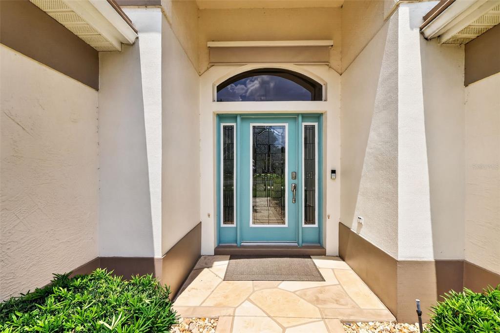A teal front door with glass panels is centered in a covered entryway with stone flooring — 522 LOMA PASEO DRIVE, LADY LAKE, FL