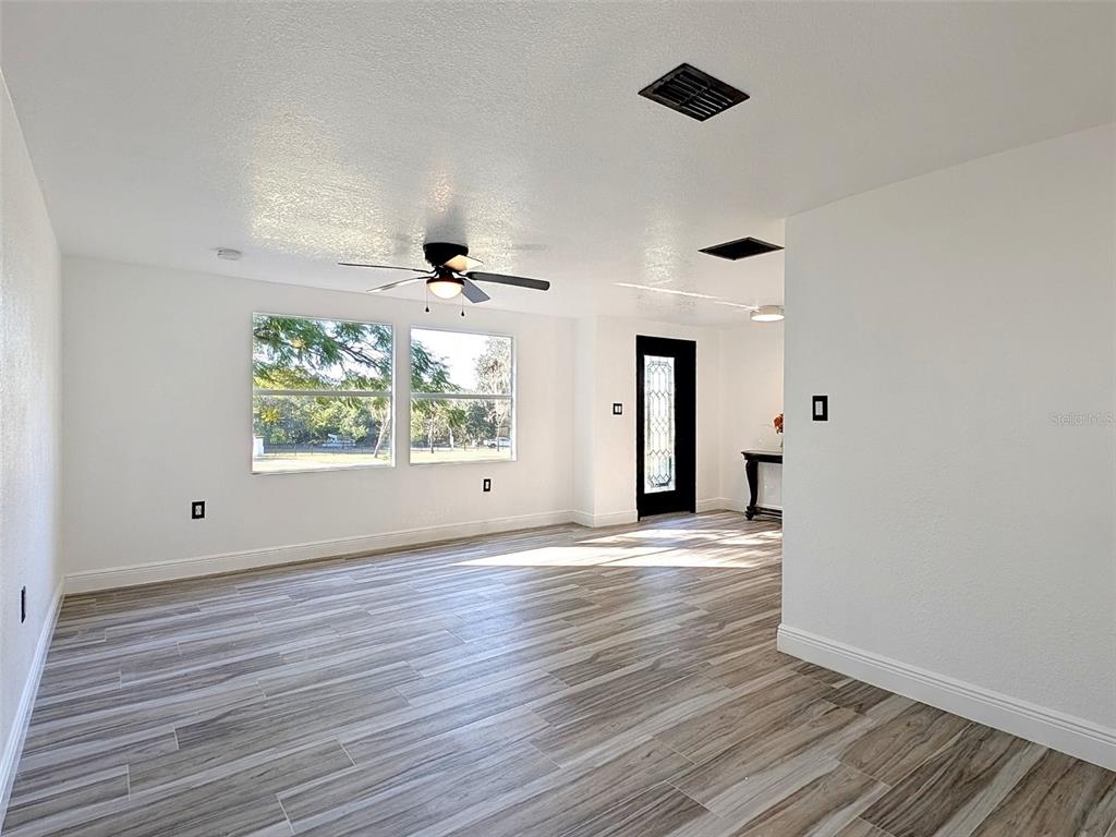 A bright living room features wood-look tile flooring, a ceiling fan, and a black front door — 15217 BAILEY HILL ROAD, BROOKSVILLE, FL