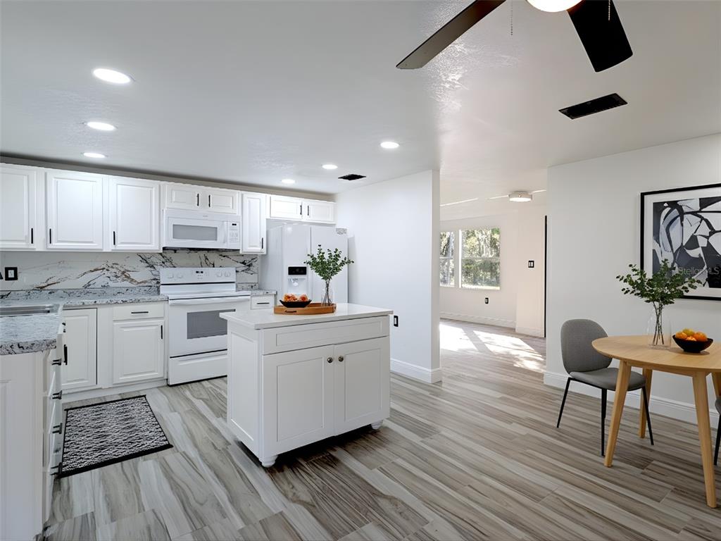 A white kitchen with an island, stainless appliances, and wood-look tile flooring — 15217 BAILEY HILL ROAD, BROOKSVILLE, FL