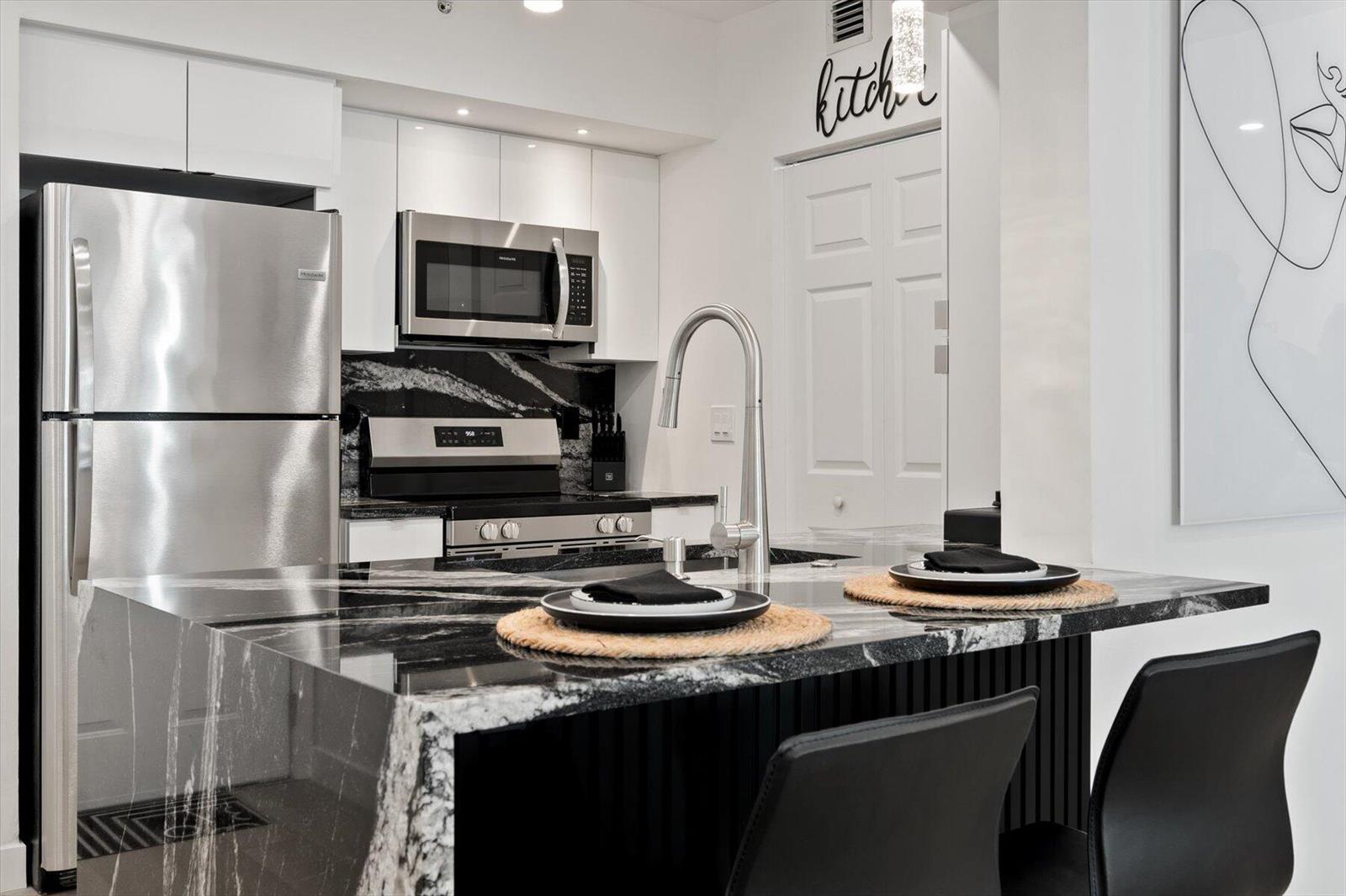 A modern kitchen features a black and white marble waterfall island, stainless steel appliances, and cabinetry — 600 S Dixie Highway # 659, West Palm Beach FL 33401, WEST PALM BEACH, FL