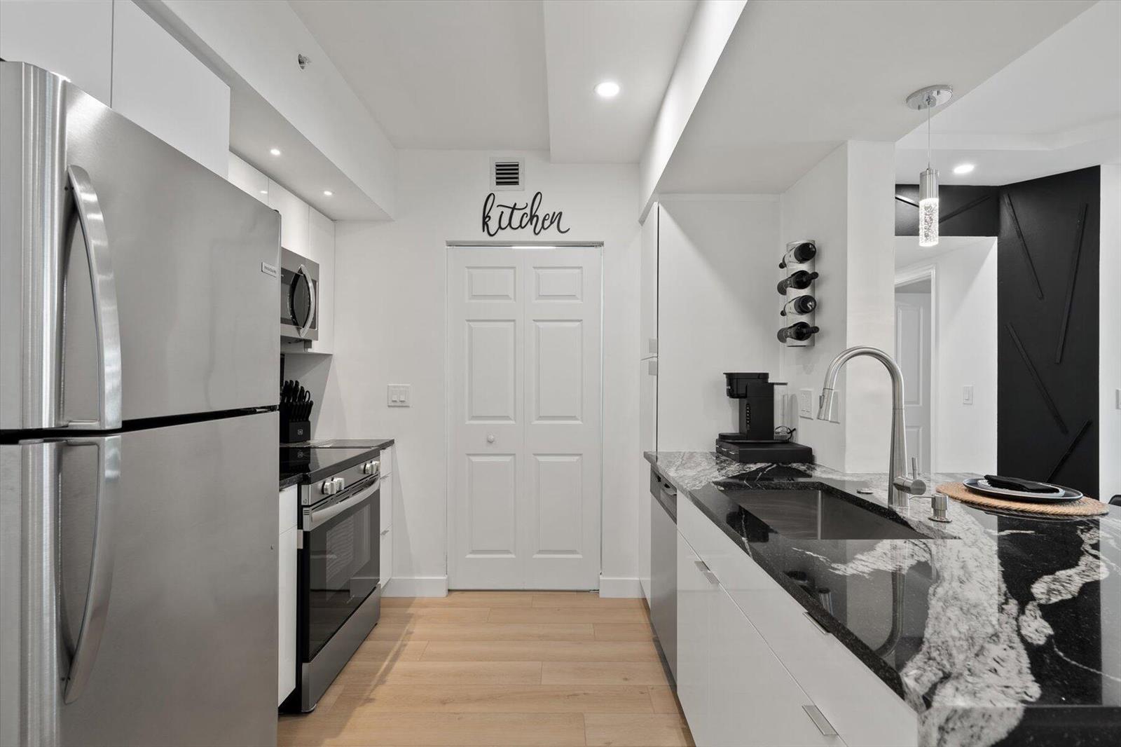 A modern kitchen features stainless steel appliances, white cabinetry, and black granite countertops — 600 S Dixie Highway # 659, West Palm Beach FL 33401, WEST PALM BEACH, FL
