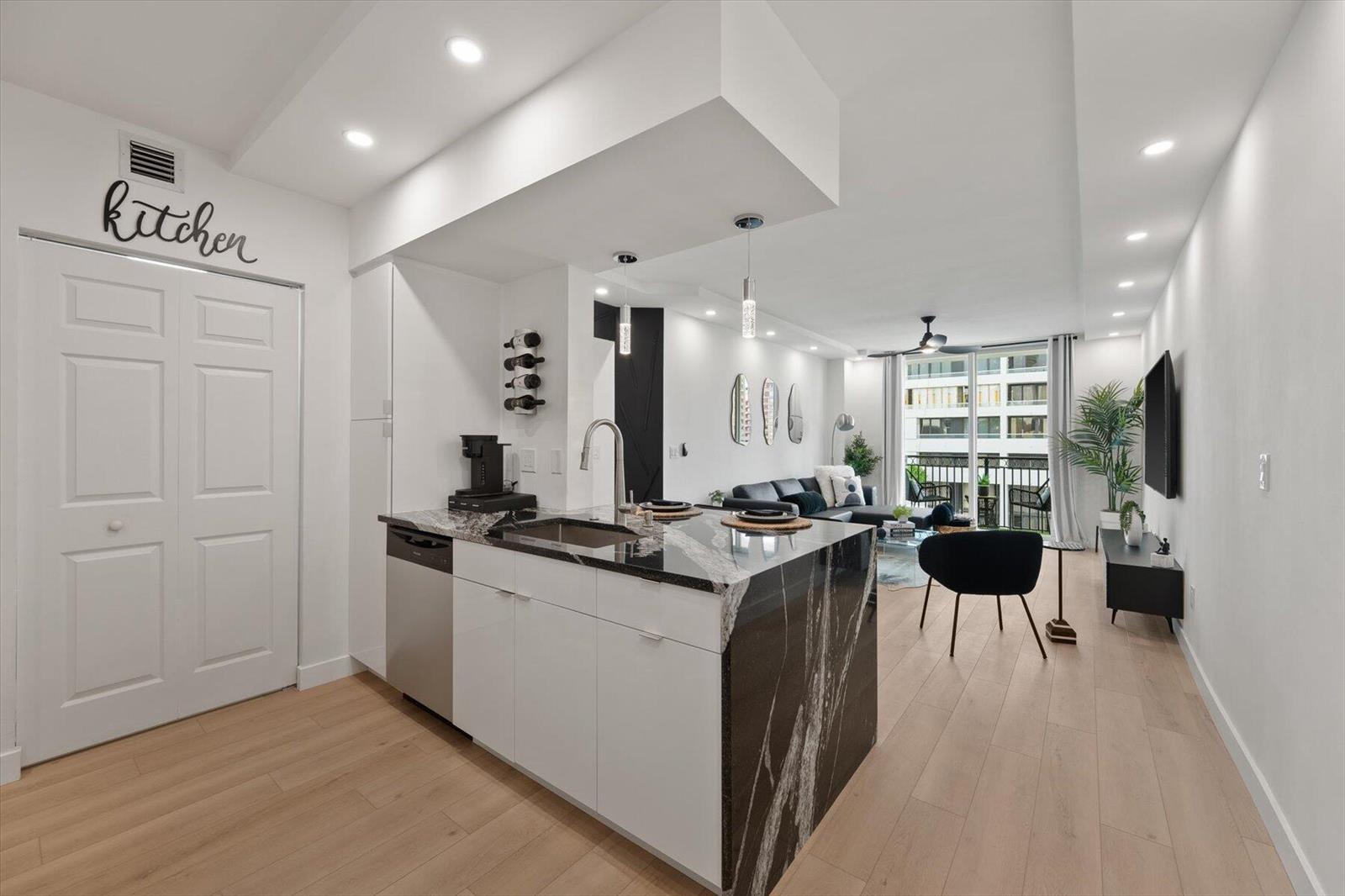 A modern kitchen with a black and white stone island overlooks a bright living area — 600 S Dixie Highway # 659, West Palm Beach FL 33401, WEST PALM BEACH, FL
