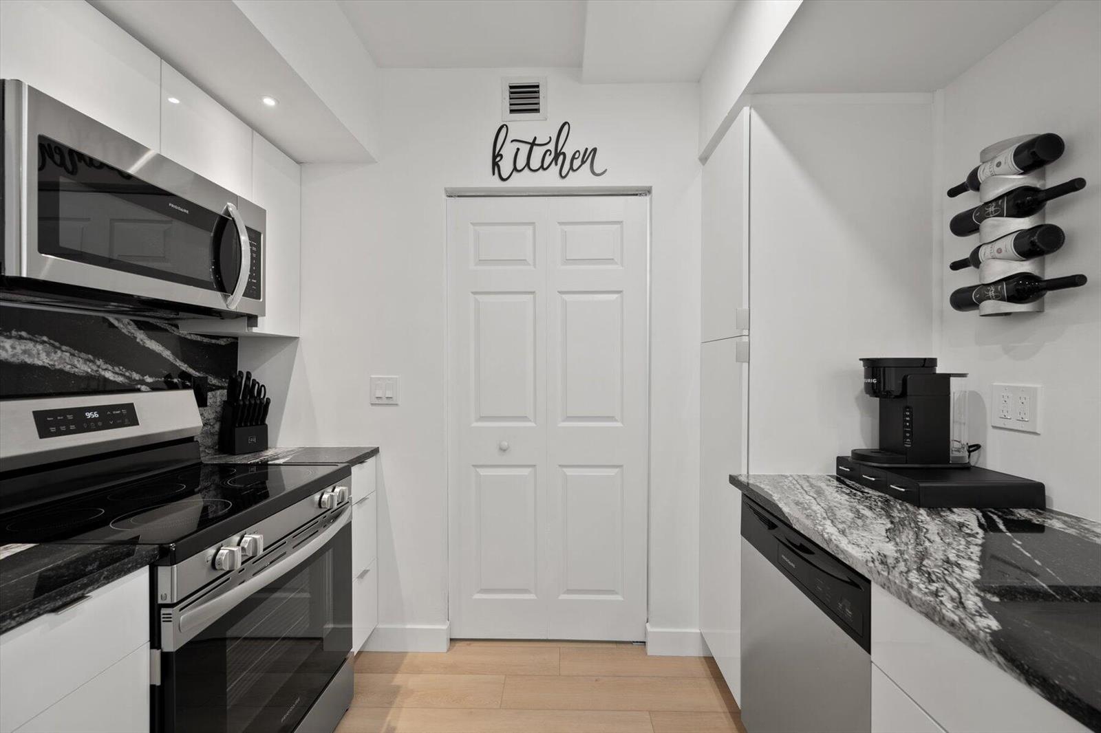 A modern kitchen features white cabinets, black granite countertops, stainless steel appliances, and a wine rack — 600 S Dixie Highway # 659, West Palm Beach FL 33401, WEST PALM BEACH, FL