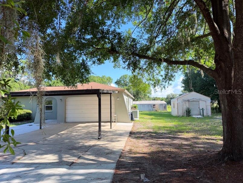A house with a carport and a detached shed sits on a grassy lot — 20801 CHISHOLM TRAIL, LAND O LAKES, FL