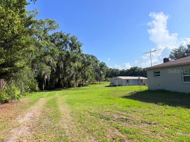 A grassy yard extends toward a detached metal building and a house with siding — 20801 CHISHOLM TRAIL, LAND O LAKES, FL