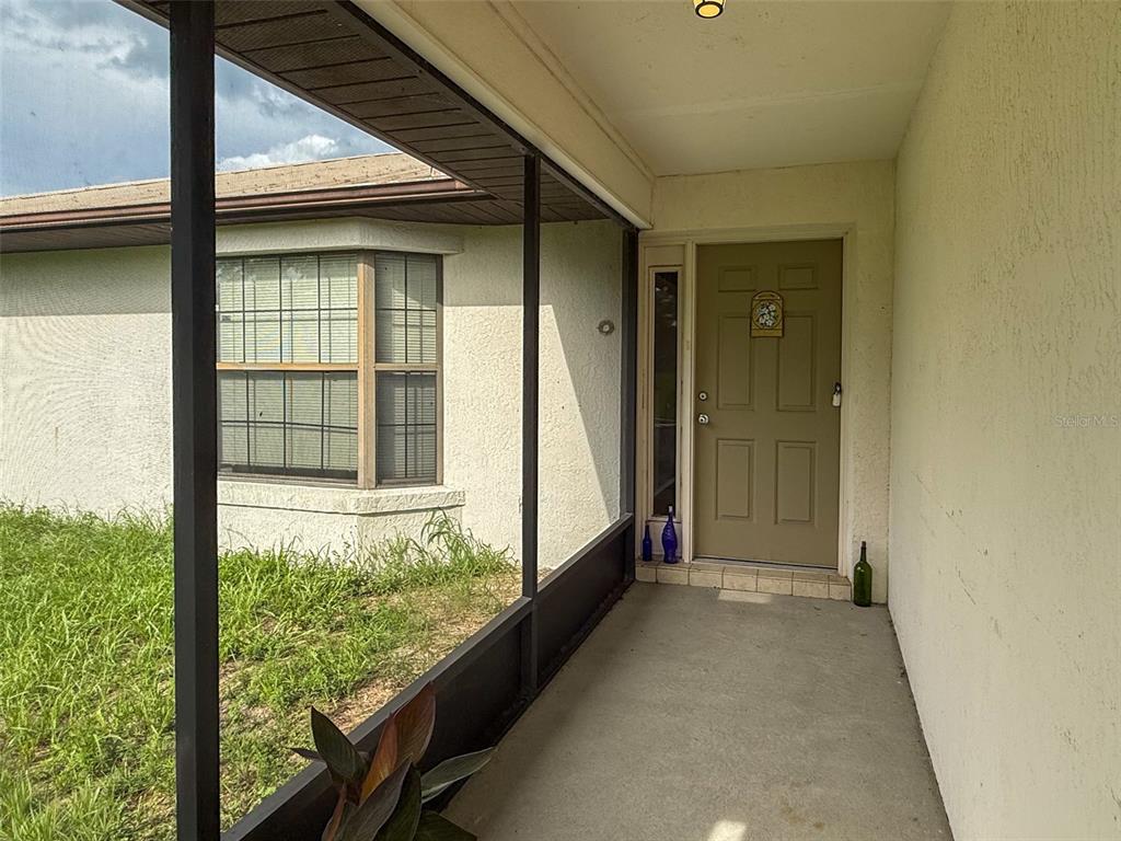 A covered front porch with a screened enclosure leads to a tan front door — 6681 CR 665, BUSHNELL, FL