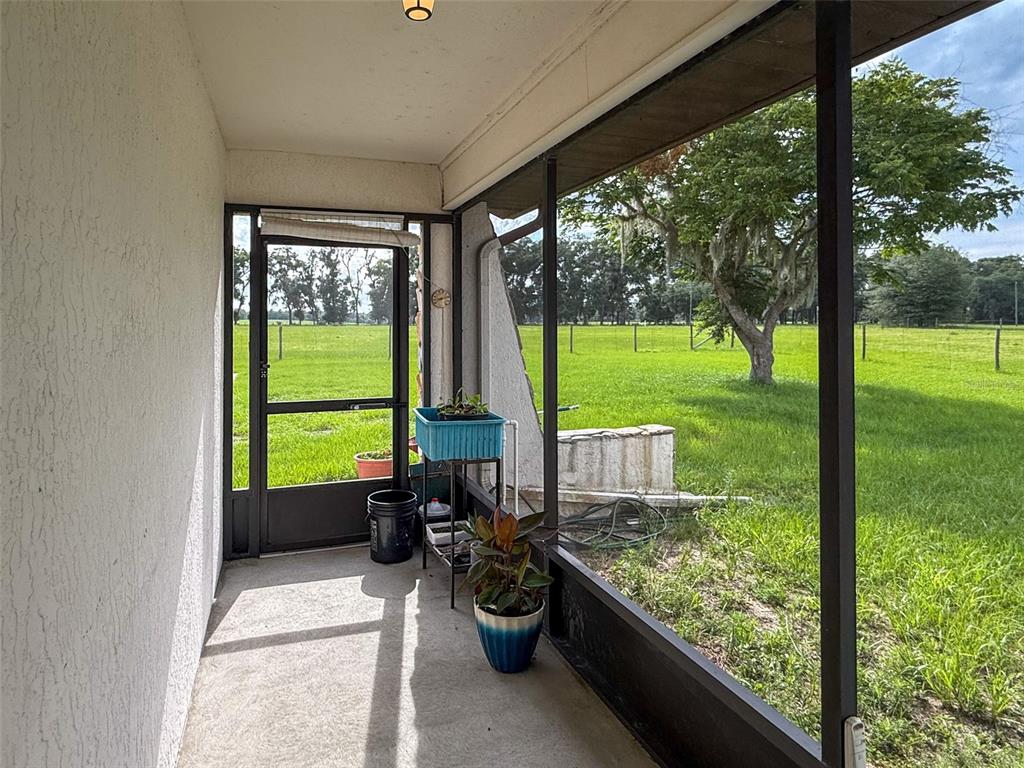 A screened-in porch features a concrete floor, a screen door, and views of a grassy field — 6681 CR 665, BUSHNELL, FL