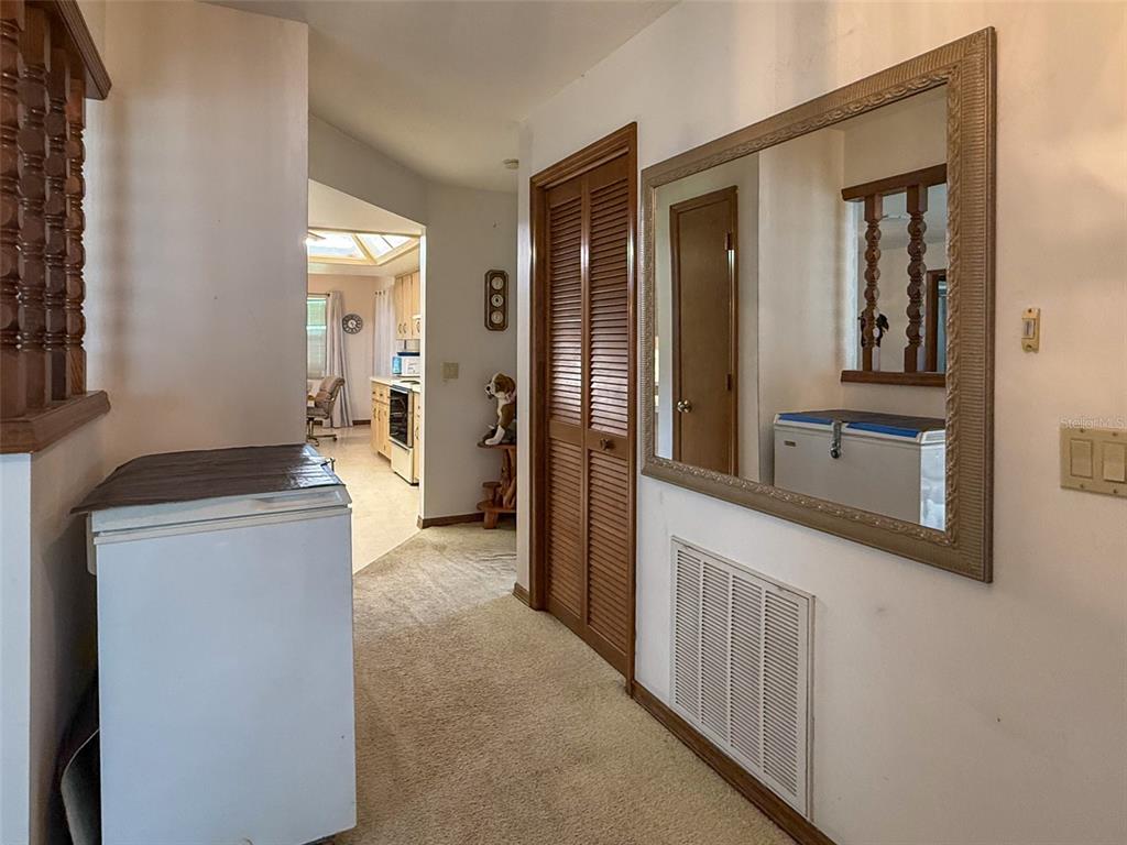A hallway with carpeted flooring, a large wall mirror, and a louvered closet door — 6681 CR 665, BUSHNELL, FL