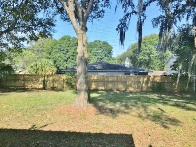 A view of a grassy backyard with a large tree and a wooden privacy fence — 4139 OLD ROAD 37, LAKELAND, FL