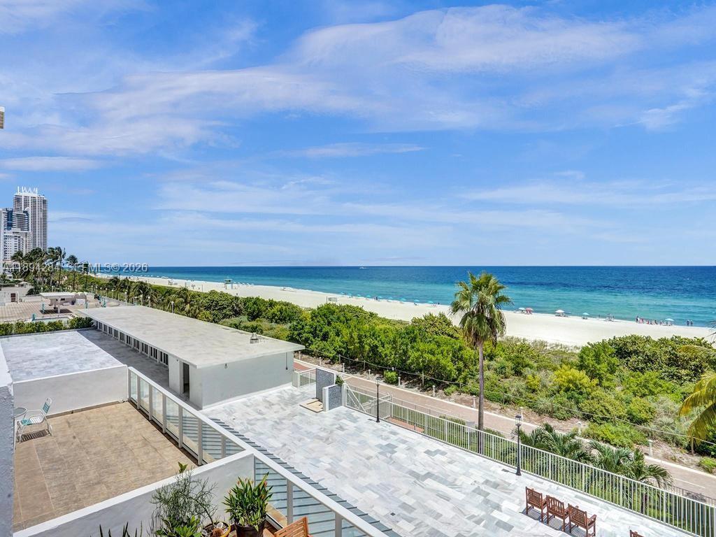 A high-angle view shows a tiled balcony overlooking a sandy beach and the ocean — 5601 Collins Ave # 504, Miami Beach FL 33140, MIAMI BEACH, FL
