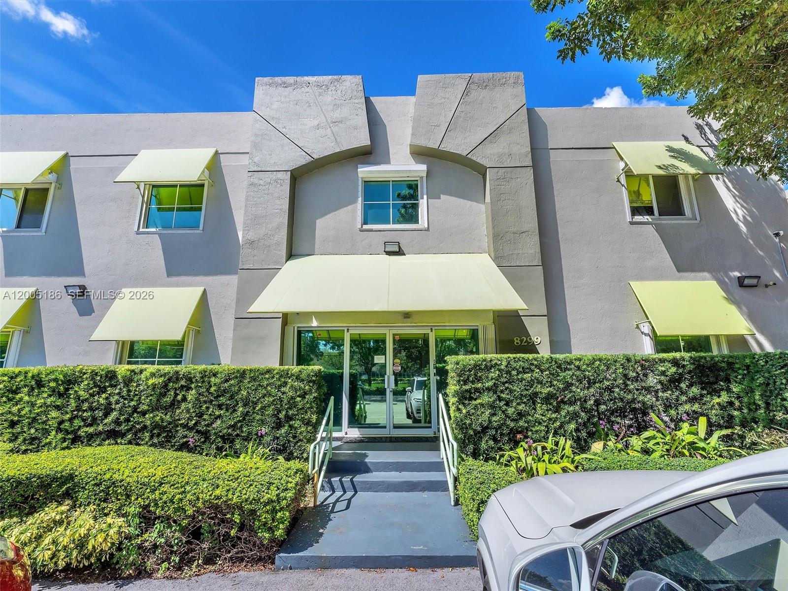 The exterior of a two-story building features light-colored walls, green awnings, and a central entrance — 8299 NW 30th Ter, Doral FL 33122, DORAL, FL