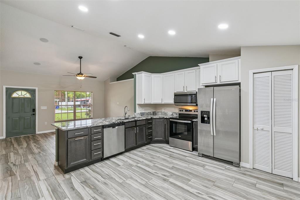 A kitchen with two-tone cabinetry, granite countertops, stainless steel appliances, and wood-look tile flooring — 1711 CHARLESTON LANE, ST CLOUD, FL