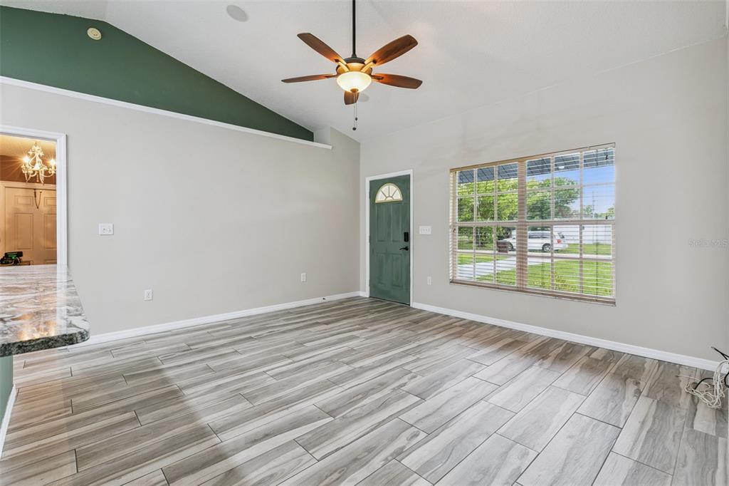 A living room with wood-look tile flooring, a vaulted ceiling, and a green front door — 1711 CHARLESTON LANE, ST CLOUD, FL