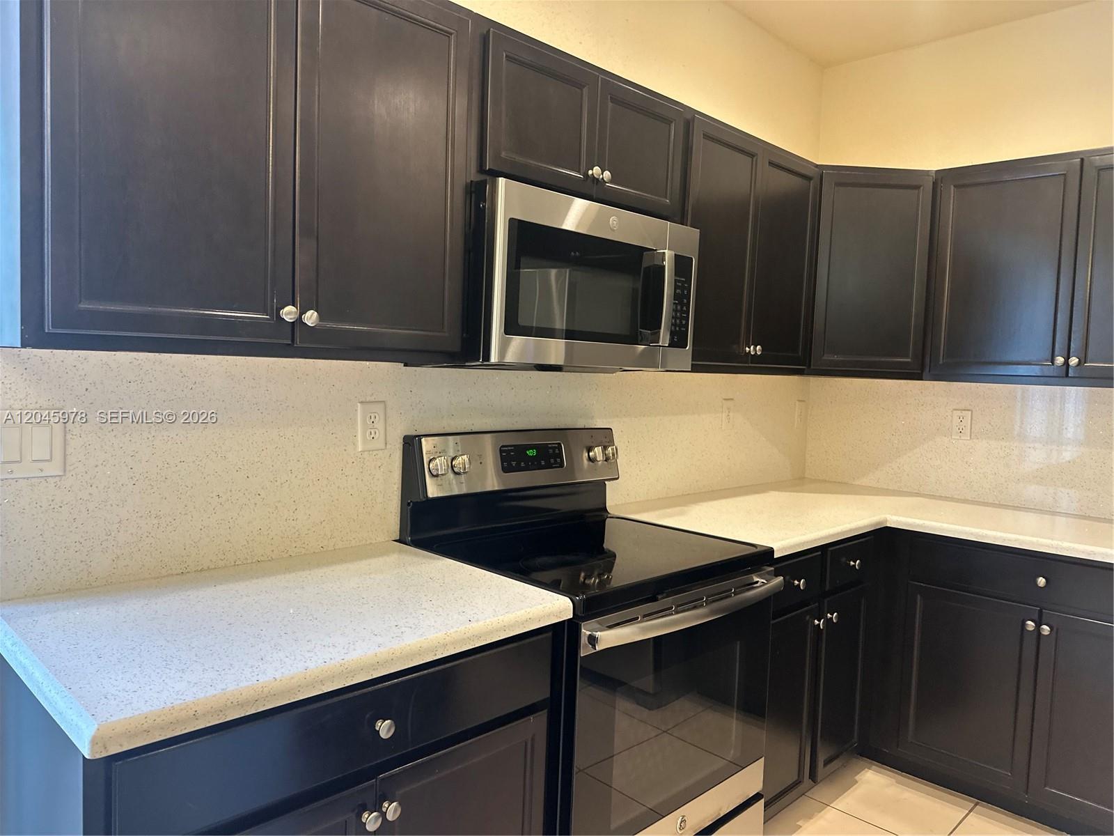 A kitchen features dark wood cabinets, stainless steel appliances, and light-colored speckled countertops — 3797 NE 2nd St, Homestead FL 33033, HOMESTEAD, FL