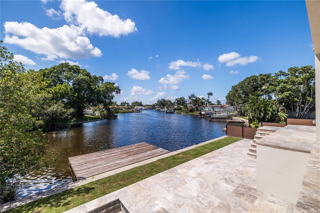 A stone patio overlooks a canal with a wooden dock and surrounding trees — 4692 DOVER STREET NE, ST PETERSBURG, FL