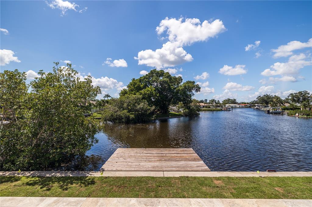 A wooden dock extends into a canal with a large tree and houses in the background — 4692 DOVER STREET NE, ST PETERSBURG, FL