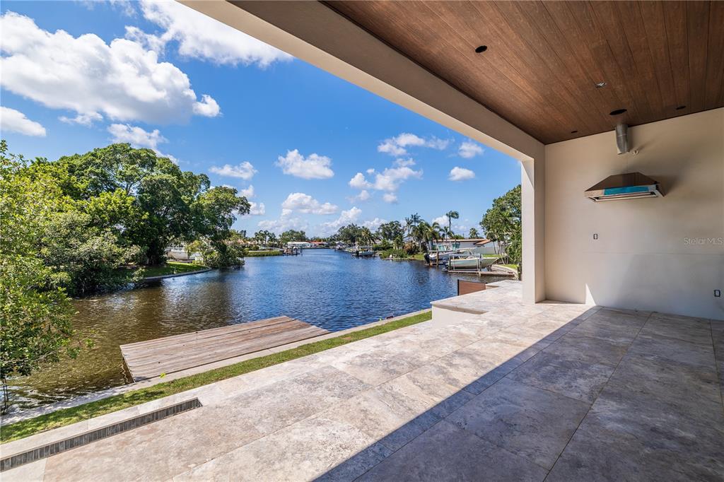 A covered stone patio overlooks a canal with a wooden dock and lush greenery — 4692 DOVER STREET NE, ST PETERSBURG, FL