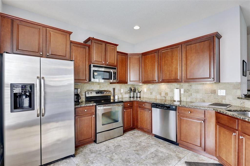 A kitchen with wood cabinets, stainless steel appliances, granite countertops, and a tile backsplash — 7001 INTERBAY BOULEVARD UNIT 257, TAMPA, FL
