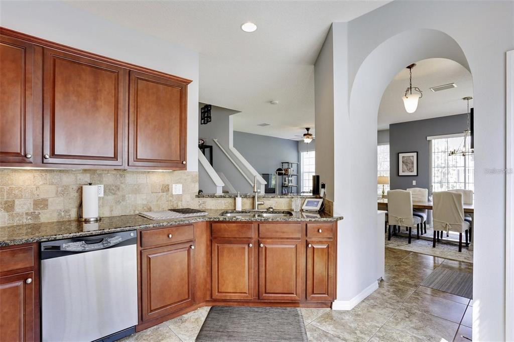 A kitchen with wood cabinets, granite countertops, and a stainless steel dishwasher overlooks a dining area — 7001 INTERBAY BOULEVARD UNIT 257, TAMPA, FL