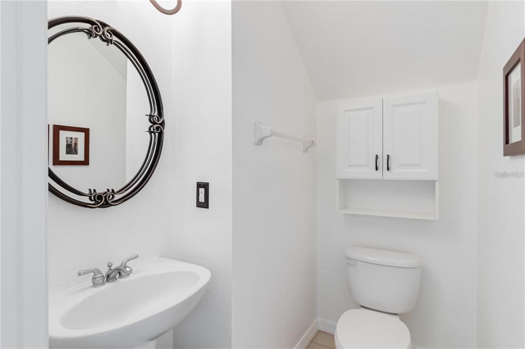 A small bathroom features a pedestal sink, a round mirror, and a white wall cabinet — 4436 CLEARY WAY, ORLANDO, FL