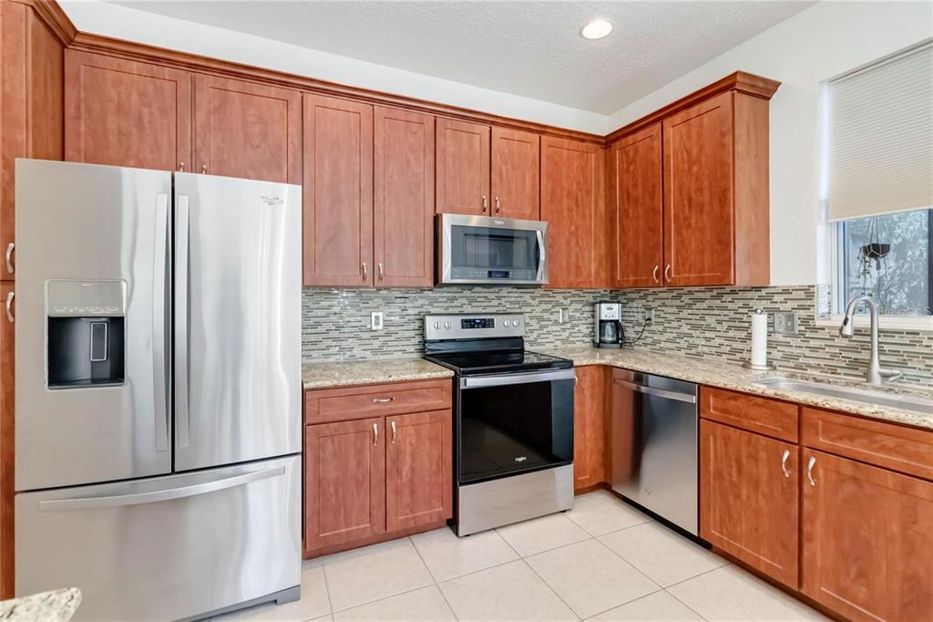A kitchen features wood cabinets, stainless steel appliances, granite countertops, and a tiled backsplash — 4436 CLEARY WAY, ORLANDO, FL
