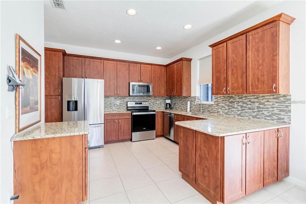 A kitchen with wood cabinets, granite countertops, stainless steel appliances, and a tiled backsplash — 4436 CLEARY WAY, ORLANDO, FL