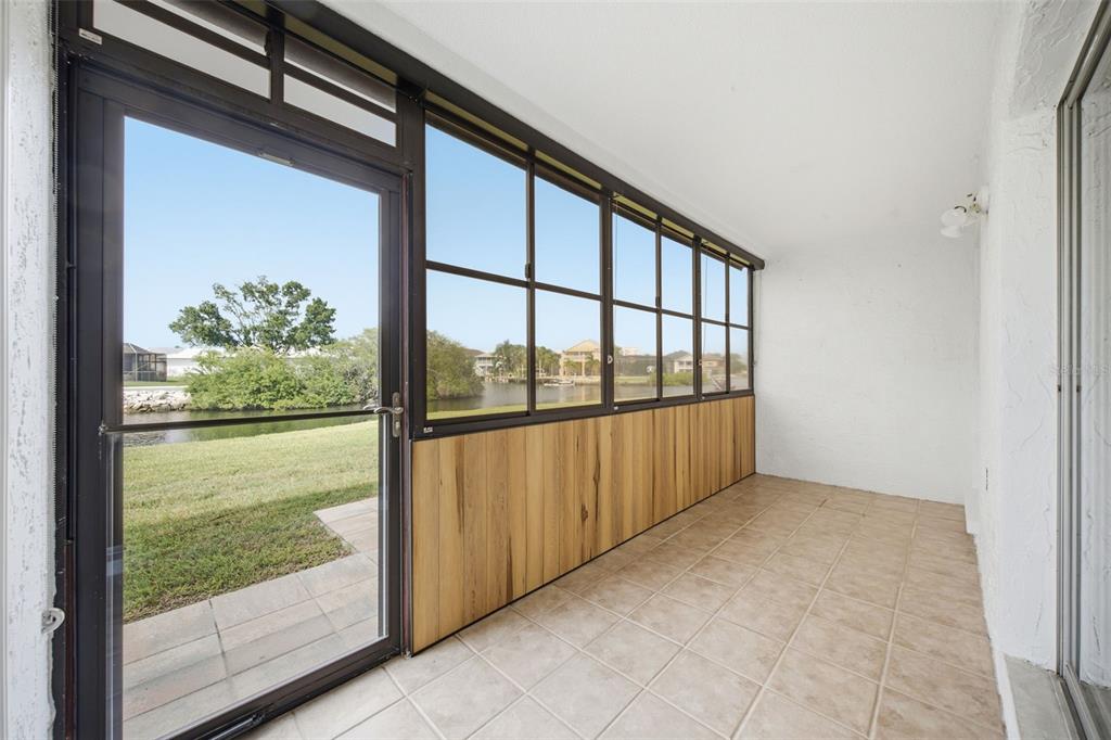 A sunroom with tiled flooring, wood paneling, and large windows overlooking a grassy waterfront area — 4555 MARINE PARKWAY UNIT 106, NEW PORT RICHEY, FL