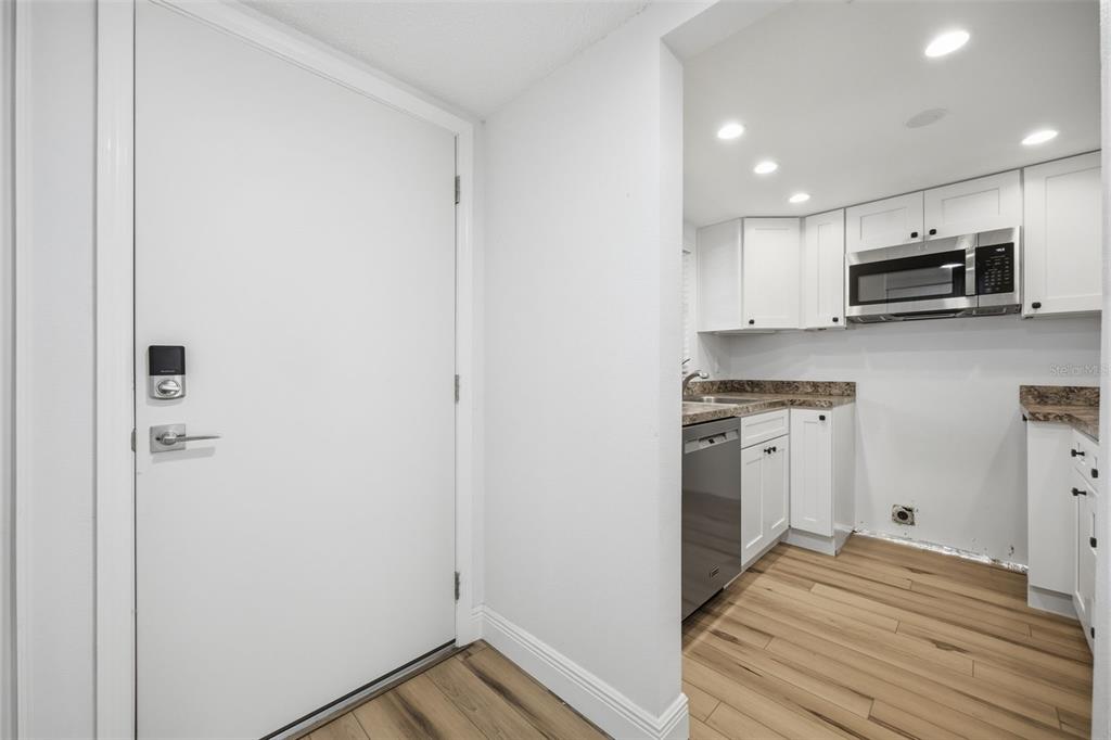 A white door opens into a kitchen with white cabinets, stainless appliances, and wood-look flooring — 4555 MARINE PARKWAY UNIT 106, NEW PORT RICHEY, FL