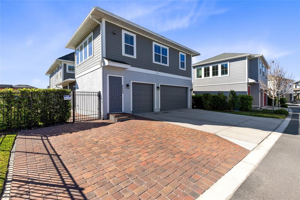 A two-story house with a brick driveway, two-car garage, and gray siding under a blue sky — 6665 BRIDGMAN STREET, ORLANDO, FL
