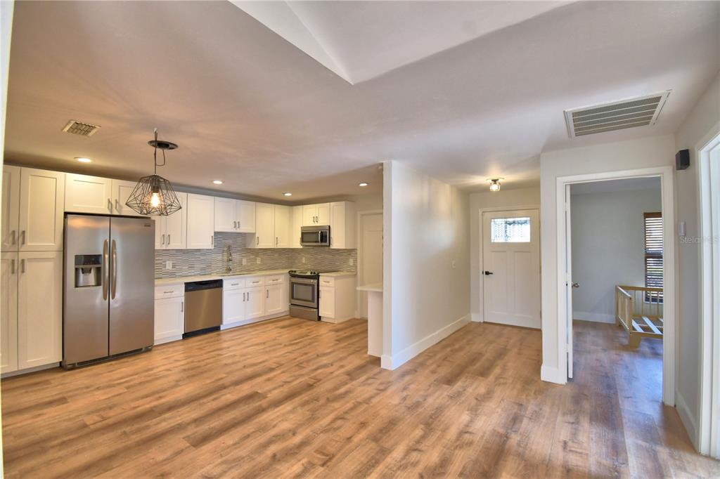 A kitchen with white cabinets, stainless steel appliances, and wood-look flooring opens to a hallway — 23 BUCK CIRCLE, HAINES CITY, FL
