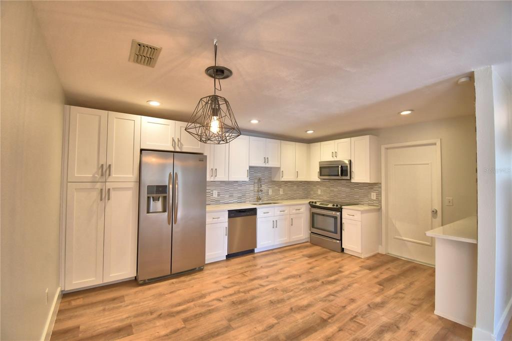 A kitchen features white cabinets, stainless steel appliances, a geometric pendant light, and wood flooring — 23 BUCK CIRCLE, HAINES CITY, FL
