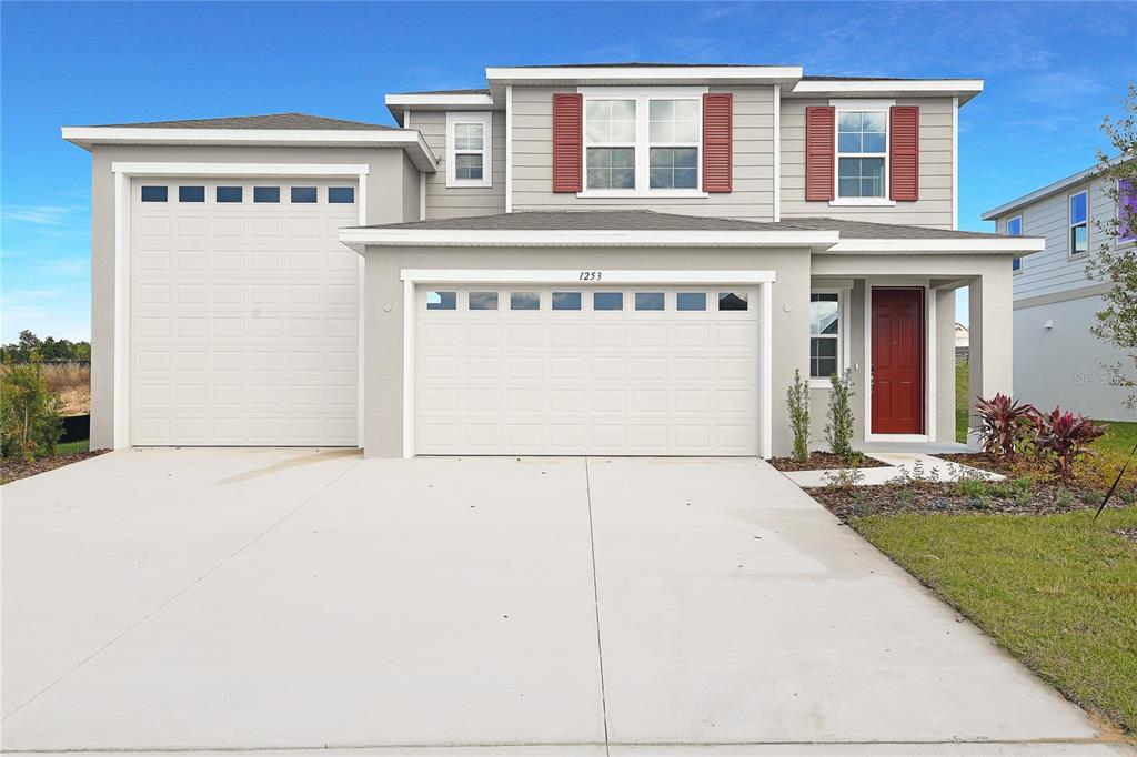 A two-story suburban house features a three-car garage, gray siding, and a red front door — 1253 DAISY HILL AVENUE, DUNDEE, FL