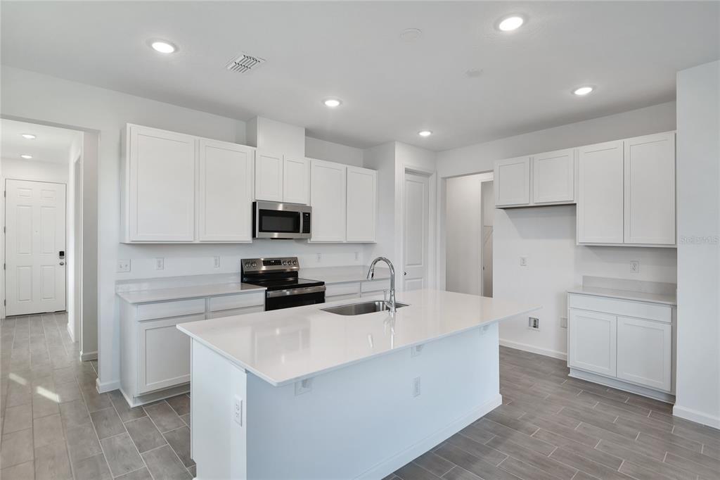 A modern kitchen features white cabinetry, quartz countertops, a central island, and gray tile flooring — 1253 DAISY HILL AVENUE, DUNDEE, FL