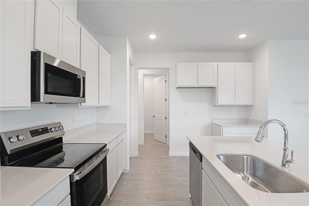 A modern kitchen features white cabinets, stainless steel appliances, quartz countertops, and gray tile flooring — 1253 DAISY HILL AVENUE, DUNDEE, FL