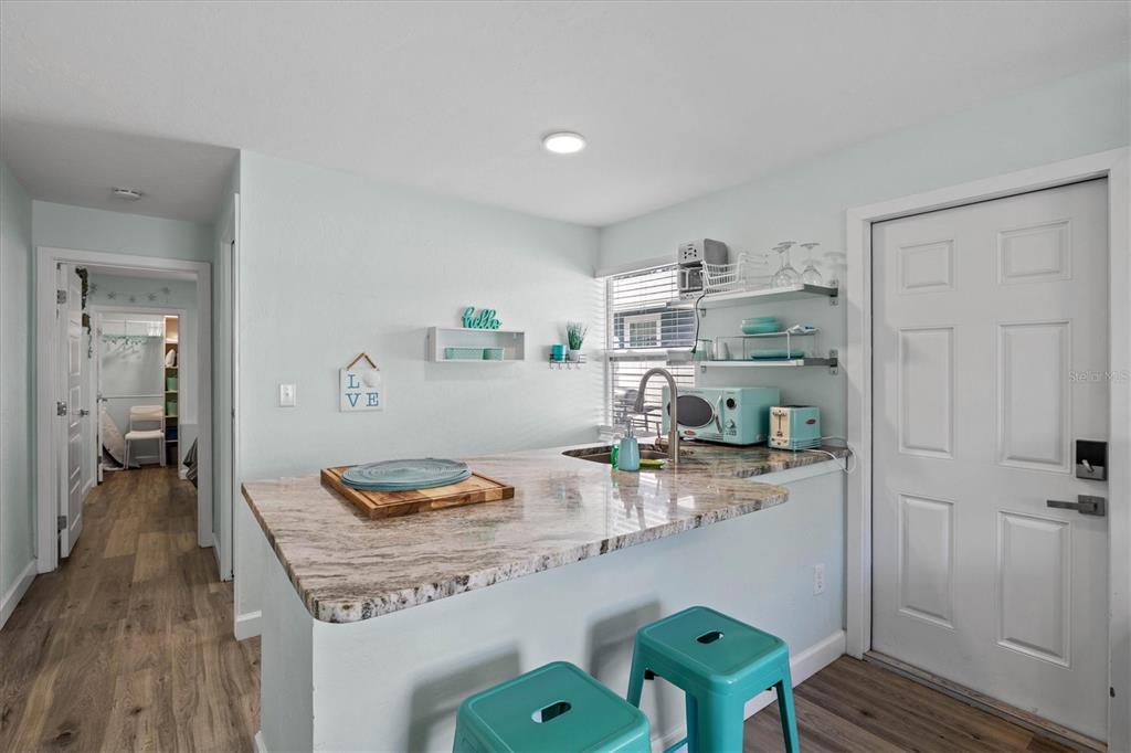 A kitchen features a granite countertop peninsula, teal stools, and open shelving near a door — 2084 GROVE STREET UNIT B, SARASOTA, FL