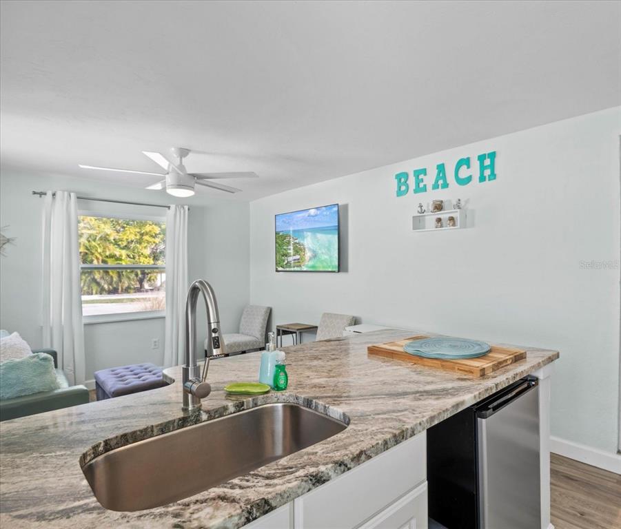 A kitchen island with a granite countertop and stainless steel sink overlooks a living area — 2084 GROVE STREET UNIT B, SARASOTA, FL