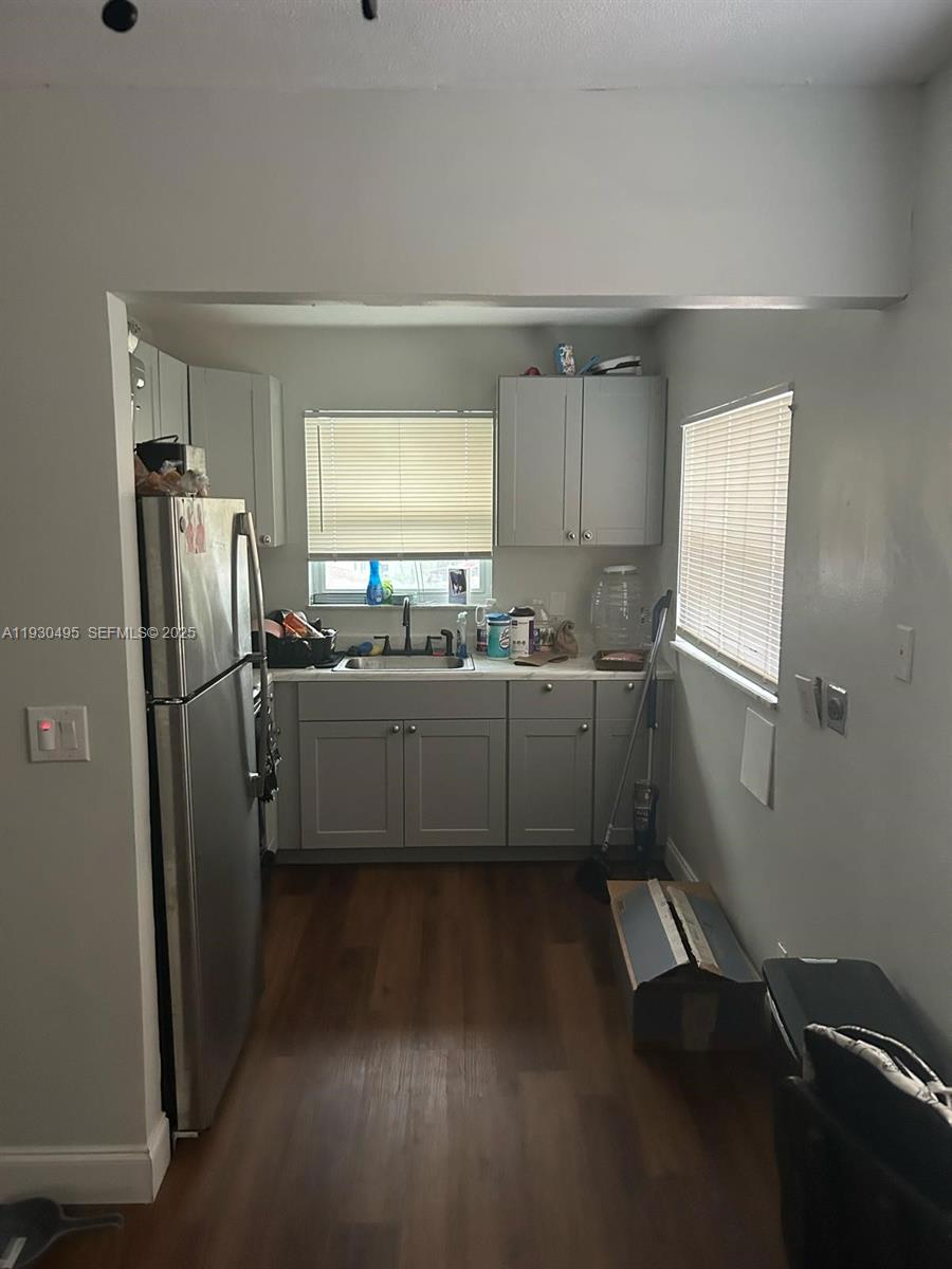 A galley-style kitchen features grey cabinets, stainless steel appliances, and wood-look flooring — 201 W Blue Heron Blvd, Riviera Beach FL 33404, RIVIERA BEACH, FL