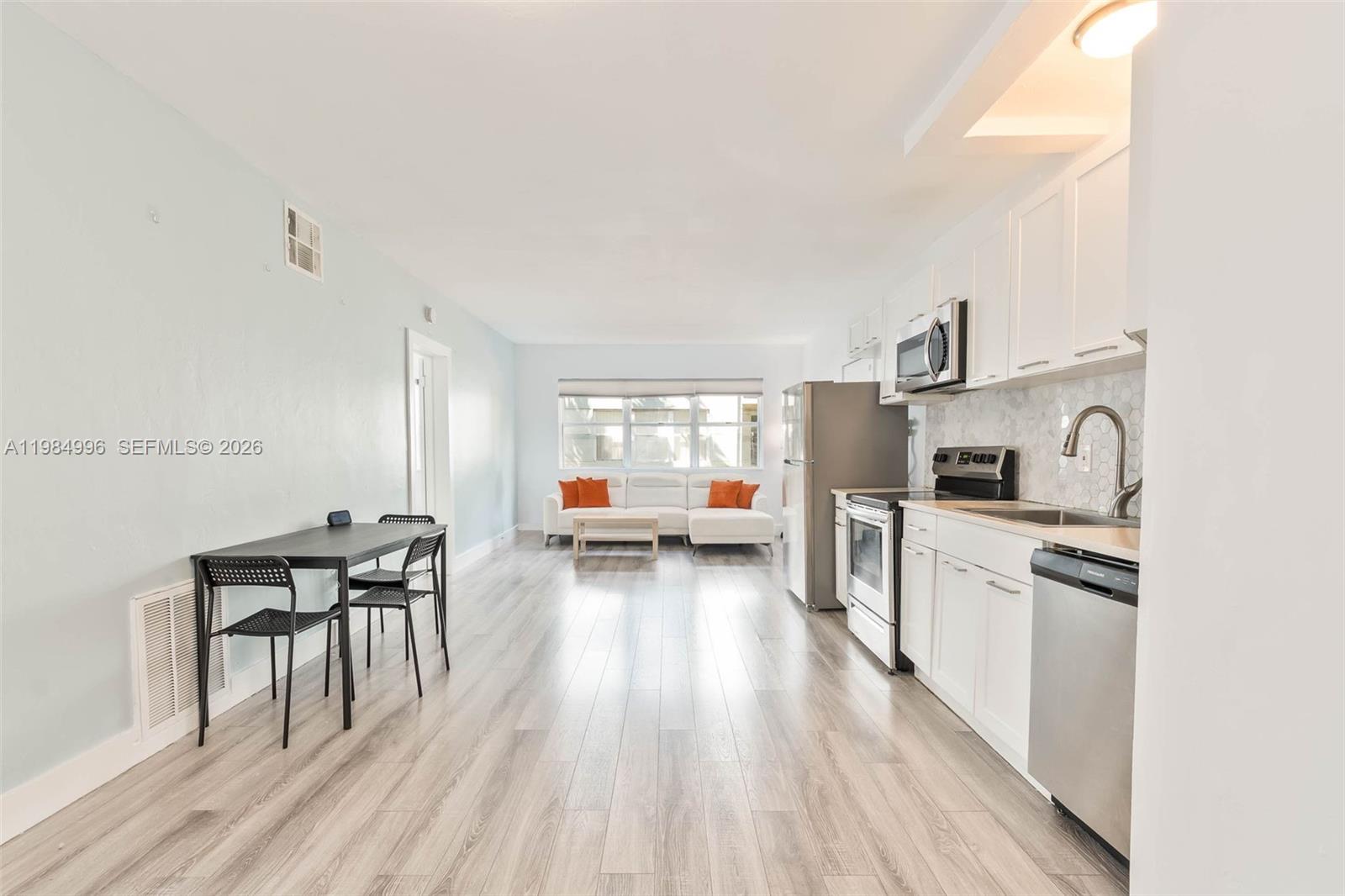 This open-concept kitchen and living area features white cabinetry, stainless steel appliances, and wood-look flooring — 1275 Marseille Dr # 35, Miami Beach FL 33141, MIAMI BEACH, FL