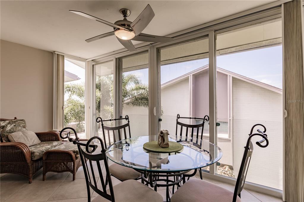 A sunroom features a glass-topped dining table, wicker seating, and large sliding glass doors — 6052 W PEPPERTREE WAY UNIT 235B, SARASOTA, FL