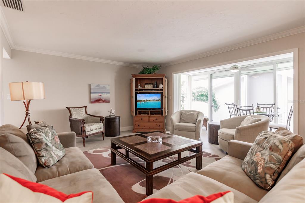 A living room features beige sofas, a wooden coffee table, and a corner entertainment center — 6052 W PEPPERTREE WAY UNIT 235B, SARASOTA, FL