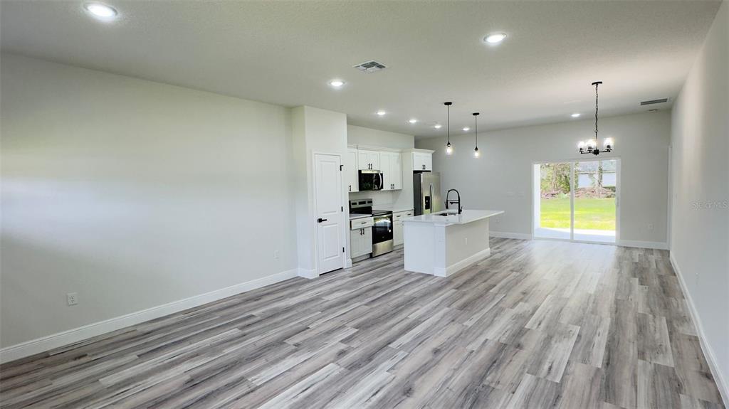 An open-concept kitchen and living area feature light wood-look flooring and white cabinetry — 3462 W CENTURY BOULEVARD, CITRUS SPRINGS, FL