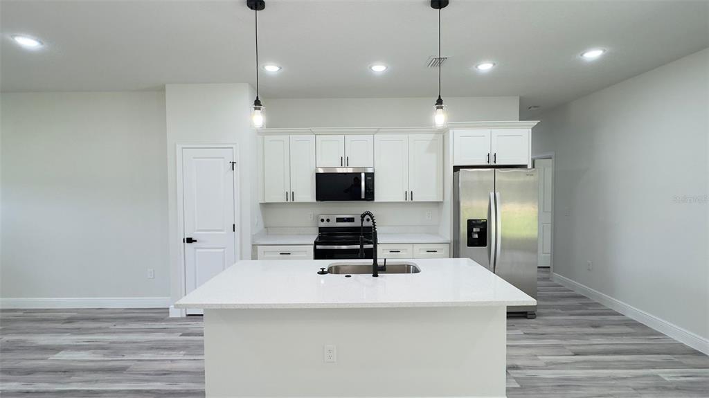A modern kitchen features white cabinets, stainless steel appliances, and a central island with seating — 3462 W CENTURY BOULEVARD, CITRUS SPRINGS, FL