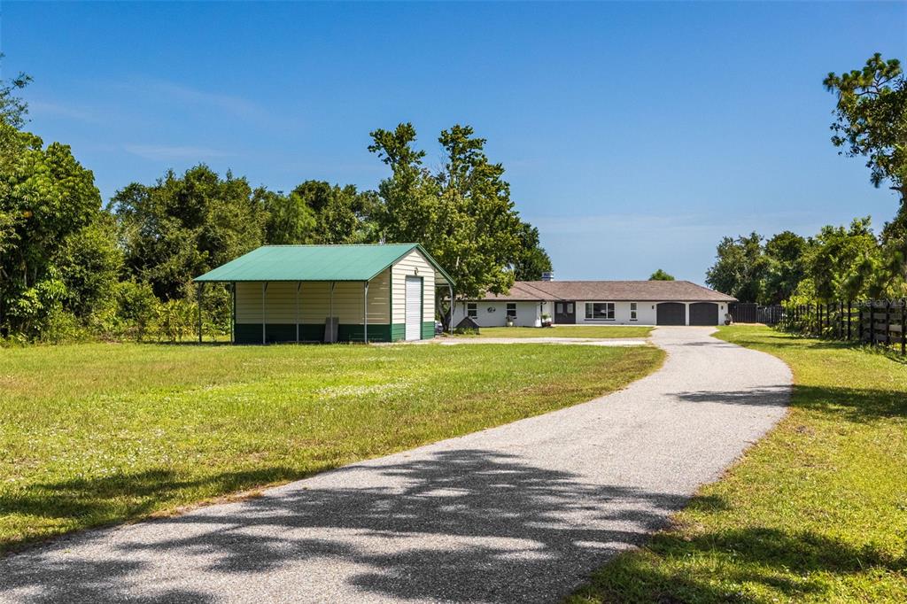 A gravel driveway leads to a single-story house and a detached green-roofed metal shed — 37951 WASHINGTON LOOP ROAD, PUNTA GORDA, FL
