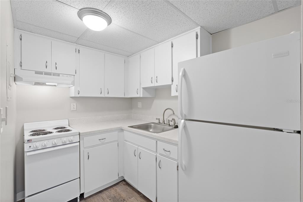 A small kitchen features white cabinets, white appliances, a stainless steel sink, and wood-look flooring — 411 1ST AVENUE N UNIT 502, ST PETERSBURG, FL